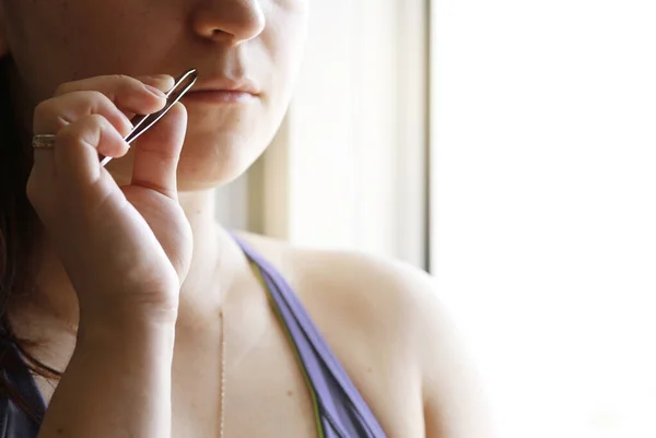 girl removes hair over her upper lip, female mustache with sharp tweezers at home. beauty treatments, hair removal.