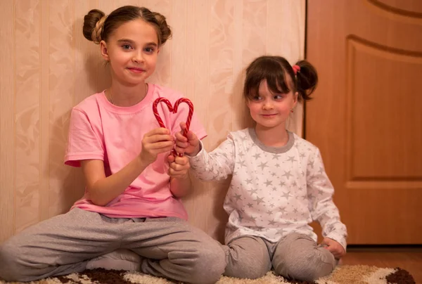 kids pajama party. funny girls in pink, white and gray pajamas with bob hairstyles play with red christmas candy canes