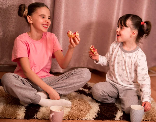 children's pajama party. funny girls in pink, white and gray pajamas with bob hairstyles eat donuts and laugh