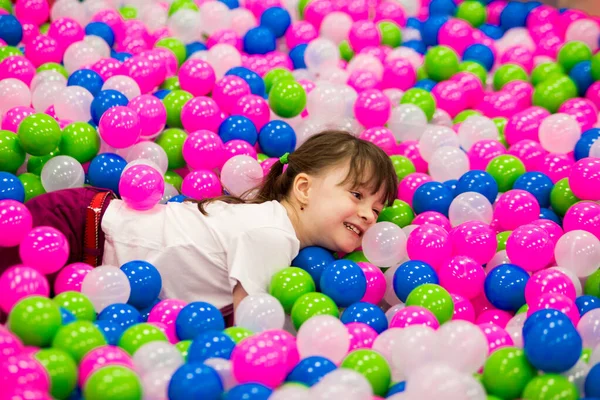 smiling girl with ponytails in a white T-shirt swims in the pool with colorful balloons on the playground room