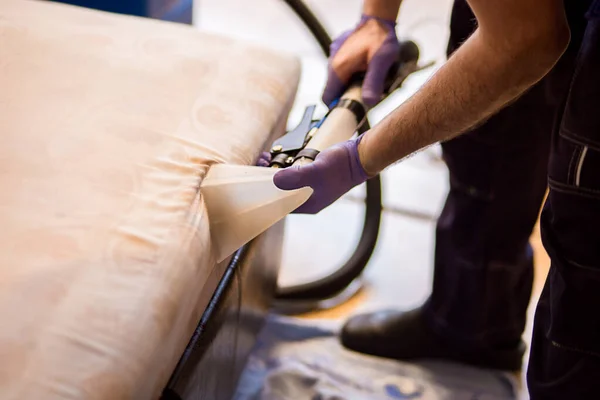 the master does a dry cleaning of the upholstery of a soft sofa using a professional washing vacuum cleaner. process photo.