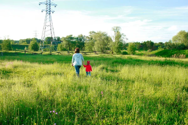 an adult woman in a gray sweatshirt and a little girl in a red sweater walk into the distance along the field. on the train plan, TV tower.