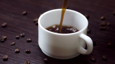 Sıcak, sade kahve ve krema, ahşap arka planda bir fincana dökülüyor.