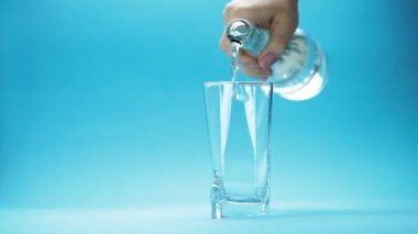 Su mavi arkaplanda bir bardağa dökülüyor.