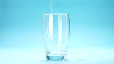 Su mavi arkaplanda bir bardağa dökülüyor.