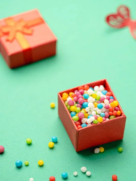 Pequeña caja de regalo llena de caramelos de colores sobre fondo verde — Foto de Stock