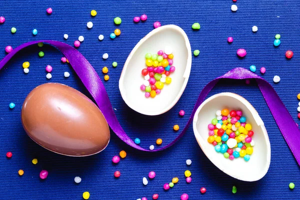 Шоколадне яйце зі стрічкою та кольоровими цукерками на синьому фоні — стокове фото
