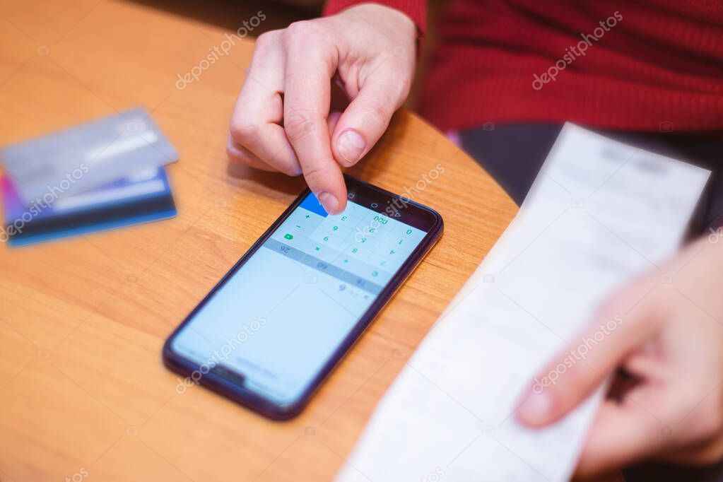 Person who calculates the total purchases from the tax receipt on his phone over a table