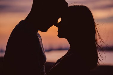 Günbatımında romantik anlar yaşayan genç bir çiftin silueti.