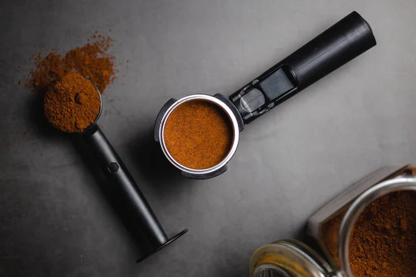 Koffiezetapparaat, portafilter met gemalen koffie en lepel over zwarte achtergrond — Stockfoto