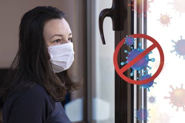 Karantinada maskesi olan endişeli bir kadın pencereden dışarı bakıyor. Virüs nüfus arasında yayılırken kendini izole etme kavramı. Virüsleri yaymayı bırak. Evde kal..