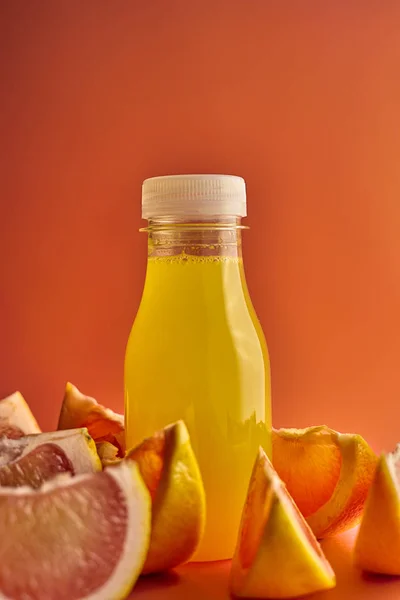 Orange juice bottle on orange background with segments of pink oranges, vertical