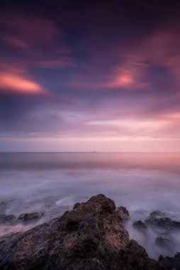 Gün batımı kıyıda kayalar ön planda dikey