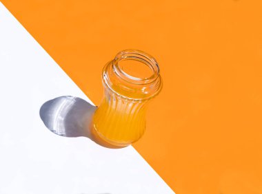 Beyaz ve turuncu zemin üzerinde portakal suyu bulunan üç çeyrek bardak iki köşegen ve merkez dışı konteynır oluşturur.