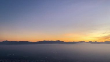 Bulutların üstünde, ufukta dağlar olan bir video. Bulutlar denizi, gün batımında dağların arasından akar..