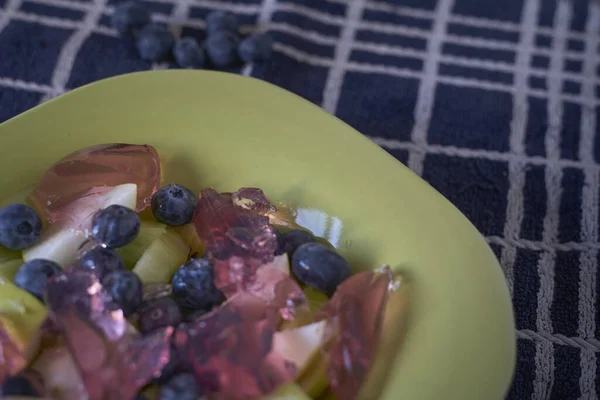 Taze meyve salatası ve kırmızı meyveli jöle. Mavi bir bez üzerinde yeşil bir tabakta. Yaklaş.