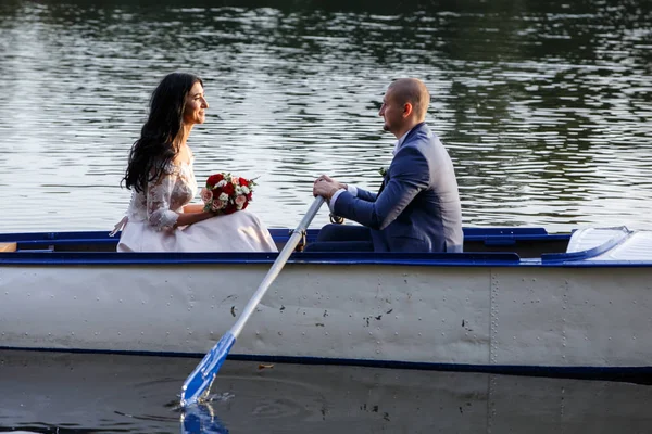 Pareja en traje de boda en el fondo del lago al atardecer, la novia y el novio. Sonrían el uno al otro. — Foto de Stock