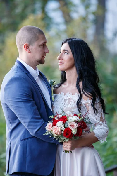 Pareja en traje de boda en el fondo del lago al atardecer, la novia y el novio. Sonrían el uno al otro. — Foto de Stock