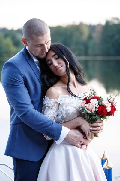 Pareja en traje de boda en el fondo del lago al atardecer, la novia y el novio. Sonrían el uno al otro. — Foto de Stock