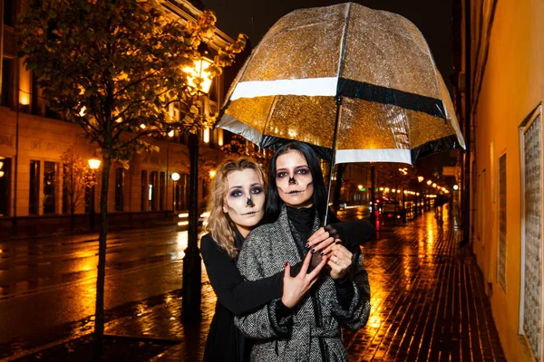 Zwei hübsche junge Weibchen spazieren beim abendlichen Halloween-Make-up auf der Straße — Stockfoto