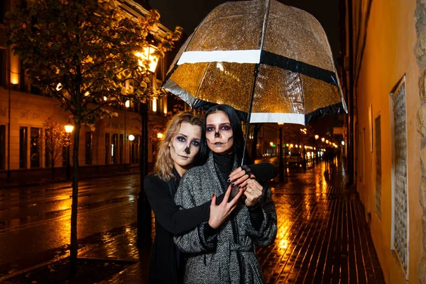 Zwei hübsche junge Weibchen spazieren beim abendlichen Halloween-Make-up auf der Straße — Stockfoto