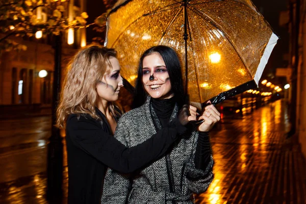 Zwei hübsche junge Weibchen spazieren beim abendlichen Halloween-Make-up auf der Straße — Stockfoto