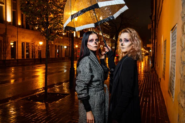 Zwei hübsche junge Weibchen spazieren beim abendlichen Halloween-Make-up auf der Straße — Stockfoto