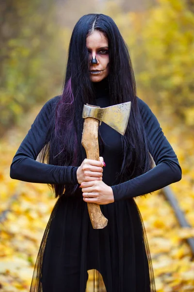 Hermosa chica con gran hacha masiva en su heand. Maquillaje creativo idea conceptual loca para la fiesta de noche de Halloween. Disfraz de carnaval pesadilla, pintura de arte corporal. Profesional cerrar foto Fotos De Stock