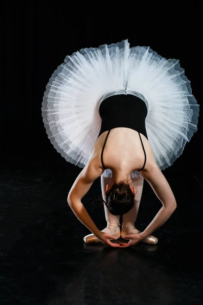 Bailarina chica posando y interpretando elementos de danza en brillante luz escénica sobre un fondo negro Fotos De Stock