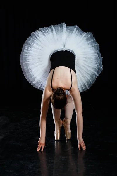Девушка-балерина позирует и исполняет танцевальные элементы в ярком живописном свете на черном фоне — стоковое фото