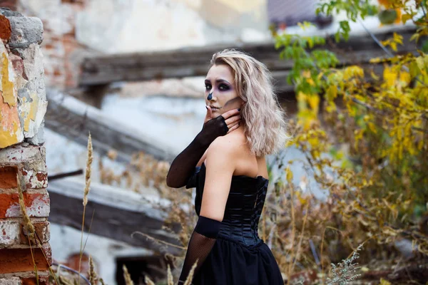 Mujer rubia en un vestido negro sexy destruyó la casa contemplando la devastación. Halloween conforman Imagen De Stock