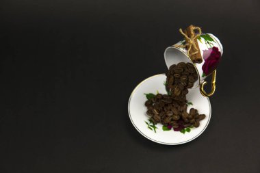 Kahve fincanından serpilmiş kahve çekirdekleri. Siyah arkaplan.