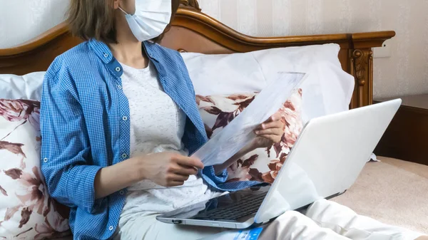 A woman in a medical mask works remotely from home on the bed. Using a computer. Distance learning online education and work