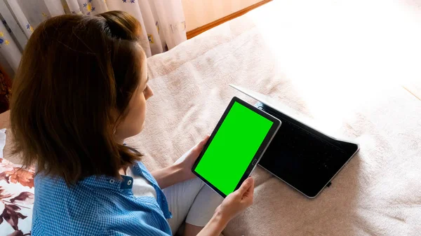 Mutlu bir kız yatağa oturur ve elinde bir tablet tutar, karantinada video iletişimiyle iletişim kurar ve evde oturur. izole edilmiş arkaplan