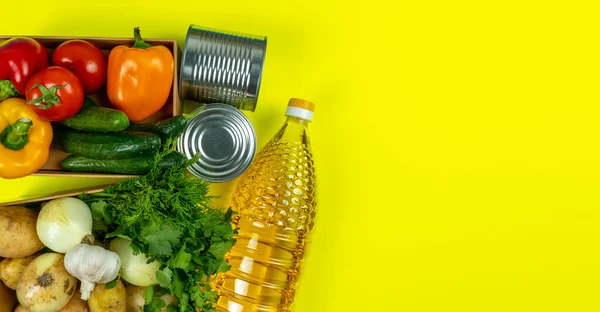Flat lay. Help products for the poor. On a yellow background. Vegetables tomatoes, peppers, butter, onions, potatoes greens, canned food, toilet paper and a paper bag. Food delivery. Pandemic.