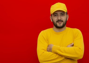 Genç teslimatçı, yükleyici, sarı şapkalı ve kırmızı arka planda tişörtlü bir işçi. metin için yer