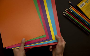 Siyah arka planda çok renkli kağıt ve kalemler tutuyordu.