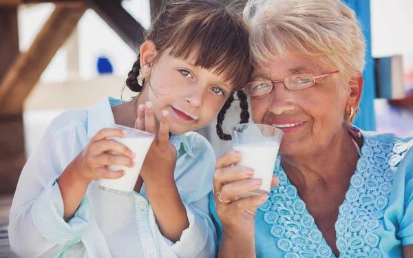 Grandmother with granddaughter drinking milk outdoors — Stock Photo, Image
