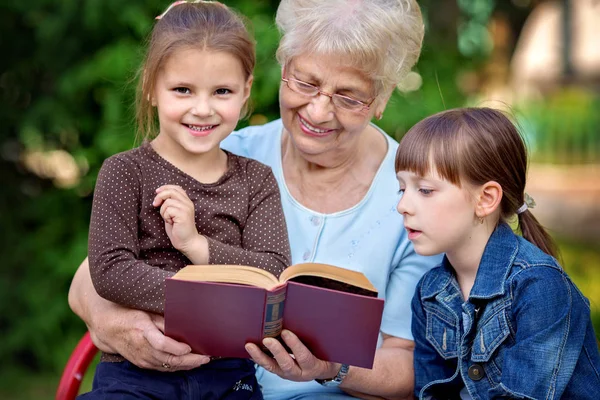 Concept d'éducation, grand-mère lisant un livre pour petits-enfants — Photo