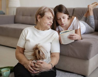 Büyükannem ve torunum kitap okuyor ve evde küçük köpekle oynuyorlar.