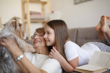 Büyükannem ve torunum kitap okuyor ve evde küçük köpekle oynuyorlar.