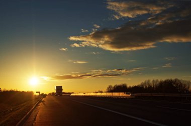 Gün batımında kırsal manzara içinde yaklaşmakta olan kamyon ile asfalt yol
