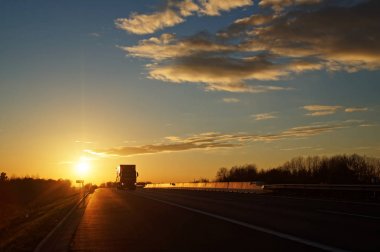 Gün batımında kırsal manzara içinde yaklaşmakta olan kamyon ile asfalt yol.