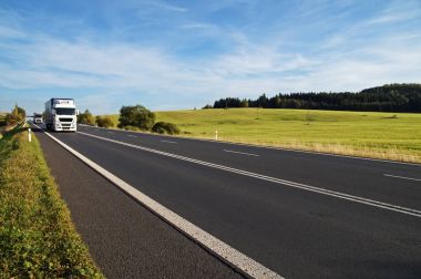 Kırsal manzara ufuk yükselen asfalt yol. Uzaktan gelen beyaz kamyon. Çayır ve orman içinde belgili tanımlık geçmiş. # Mavi gökyüzü ve beyaz bulutlar ile güneşli gün.