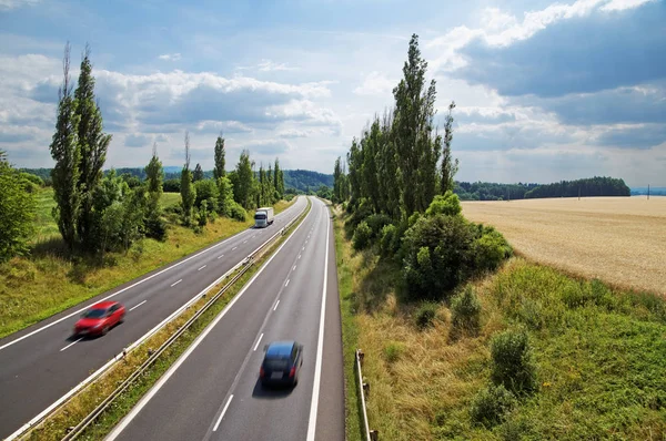 Country landscape with highway leading poplar alley next to a cornfield. Motion blur speeding cars. White truck coming from afar. View from above. Summer sunny day. — Stock Photo, Image