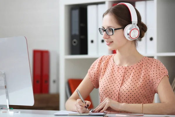 Vrouwelijke student met een koptelefoon muziek luisteren en leren. Houd de greep in zijn hand en kijken naar monitor — Stockfoto