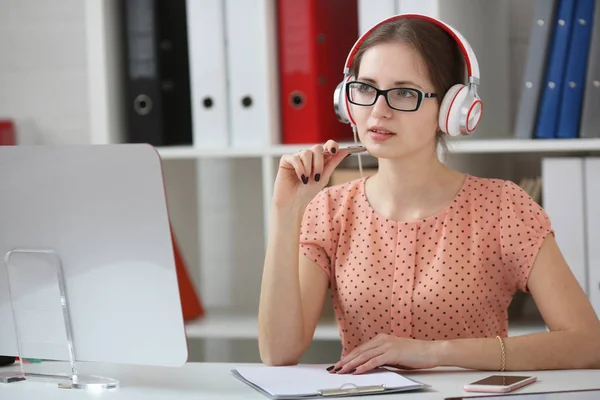 Prachtige vrouwelijke student met een koptelefoon muziek luisteren en leren. Houd de greep in zijn hand en kijken naar monitor — Stockfoto