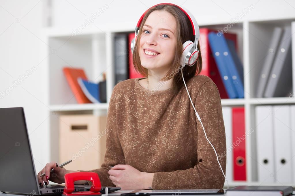 Beautiful female student with headphones listening to music and learning. Looking camera.