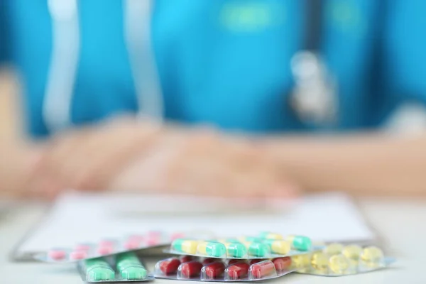 Płyty z tabletki leżące na stole. Na tle lekarz medyczny szlafrok, Zdjęcie z głębi pola — Zdjęcie stockowe