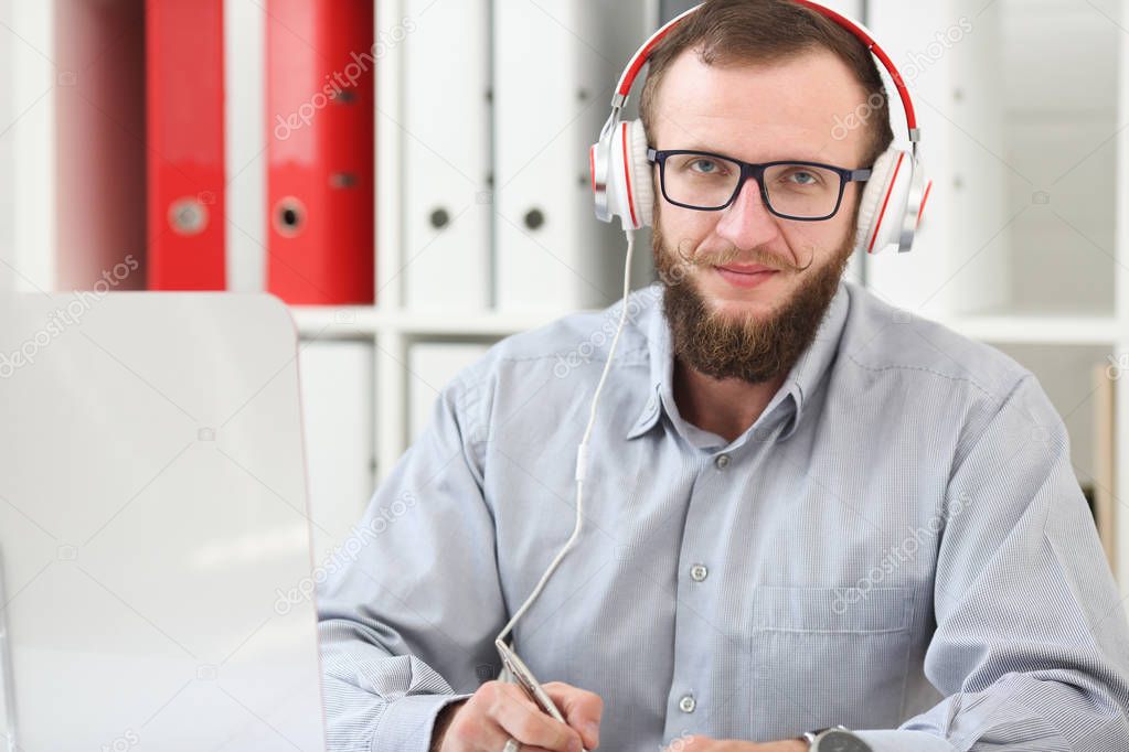 A man in headphones listens to music and learns online. Makes notes in a notebook and looks at the camera